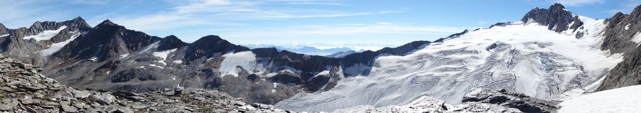 The panoramic view shows the last Austrian mountain ridge before the Italian border. Here, the ice surfaces of the Langtaler Ferner on this side of the ridge stretch up westwards to the Annakogl, a mountain peak at over three thousand three hundred metres. Apart from the azure sky, there are hardly any colours to be seen up here. The rock shines in shades of anthracite-grey, interrupted only by patches of white snow and ice. The mountains of the Italian Alps in the background fade with increasing distance.